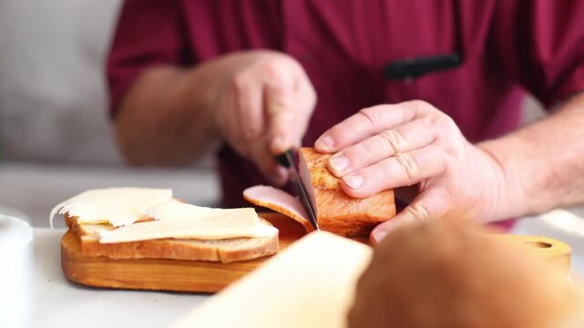 Close up of hands slicing cooked sausage and layering it onto buttered bread with cheese, methodical breakfast sandwich prep at a home table.