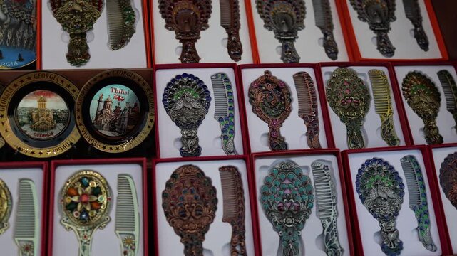 Decorative souvenir mirrors and combs with ornate patterns displayed in market handcrafted accessories traditional Georgian design colorful metal craftsmanship