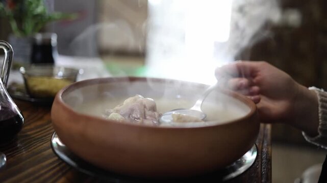 Steaming Georgian khash bone broth served in clay bowl on rustic wooden table traditional slow cooked soup creating authentic Caucasian cuisine atmosphere