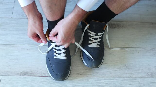 Close up of hands tying white laces on worn navy sneakers, capturing a grounded, everyday ritual of preparation, comfort, and quiet readiness.