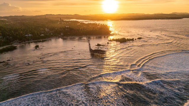 Aerial view of the iconic Cloud 9 wooden boardwalk in General Luna, Siargao, Philippines. The golden evening light reflects on the waves of the famous surfing destination