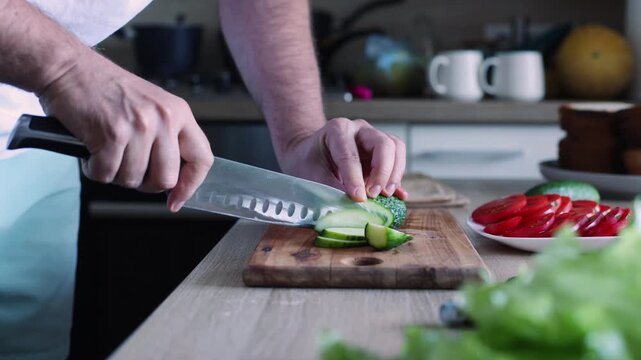 A man slices a cucumber with a santoku knife on a wooden board, in a bright kitchen, embodying mindful meal prep, freshness, and home cooked care.