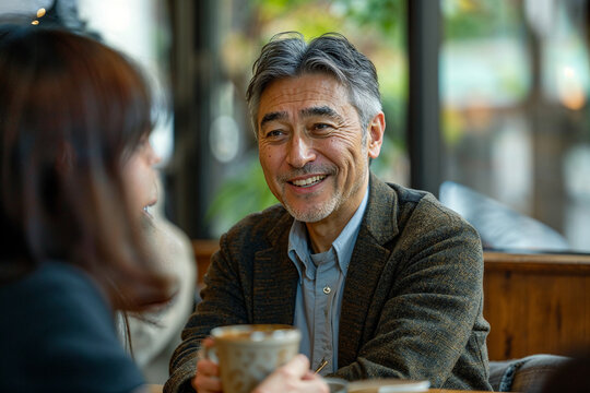 Warm and approachable Japanese male business leader in his mid-50s, looking around 55 years old, prominent grey hair, smart casual style with dark olive knit blazer, sharing a natural conversation and