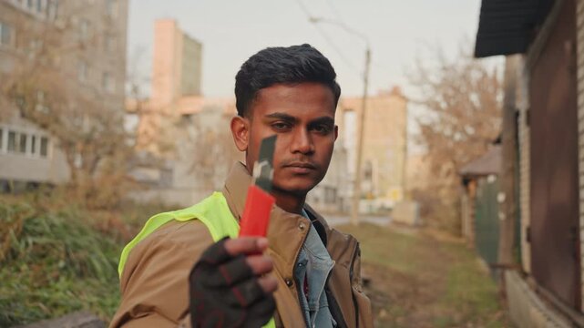 Action repair technician holding tool young male field technician wearing gloves and highvisibility vest presents red tool toward camera, intense focused stare, closeup on gloved hand and tool tip,