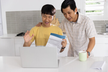 Asian family members reviewing documents on laptop at home kitchen with green mug and envelope © wavebreak3