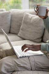 African American man on sofa typing on laptop holding mug in green top, copy space © wavebreak3