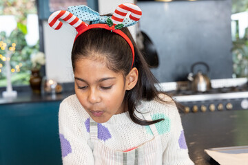 Indian child girl at kitchen counter leaning pursing lips cooling food kettle apron headband lights © wavebreak3