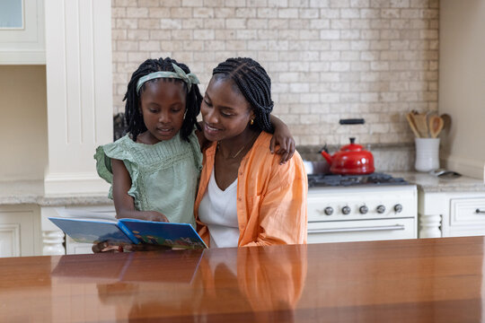 African American mother and child in green dress sitting at kitchen counter reading blue book