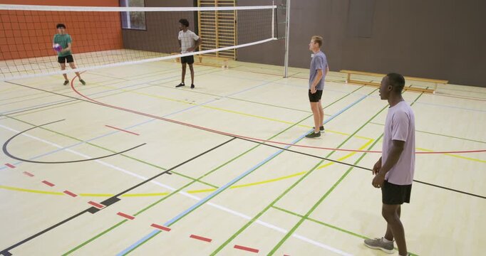 Five male players light purple tee receiving far-left serve over net to continue rally, copy space