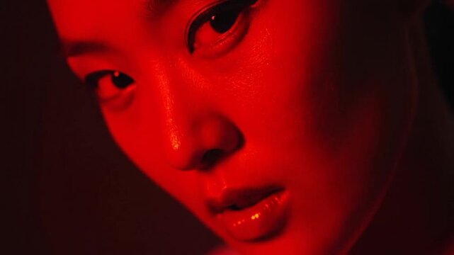 Close-up of a person's face illuminated by intense red light, with dramatic eye makeup