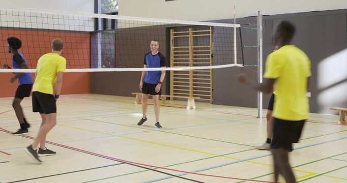 Yellow adult male team starting rally, striking ball across net in school gym, trying to score