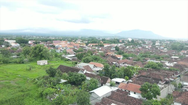 Aerial 4K view of a dense Indonesian suburban village with red-tiled roofs and distant mountains.