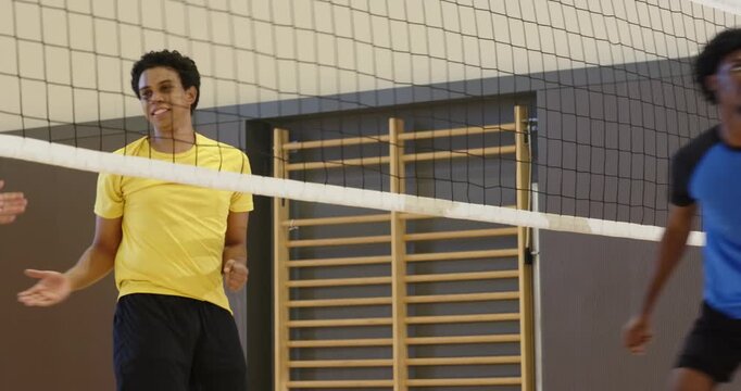 Yellow-shirted men reacting to setter lifting ball, blocking spike, defending point at gym net
