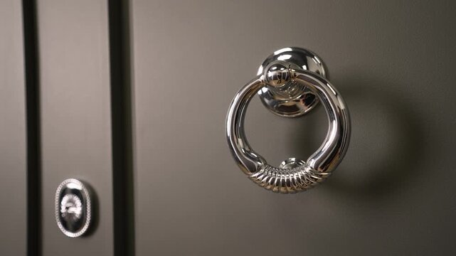 Closeup of a shiny, chrome ring handle on a dark gray cabinet door. The camera slowly zooms out, revealing classic, elegant furniture hardware and design