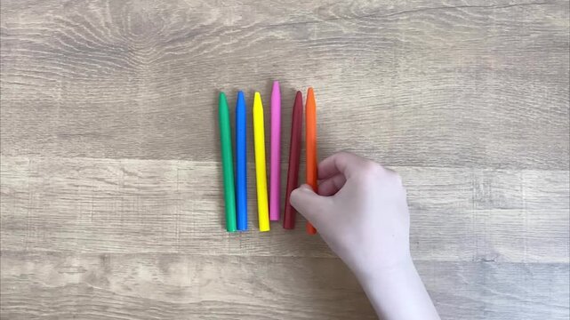 Placing the sixth colorful crayon in a row on wooden table, counting and sequencing concept for children, slow motion