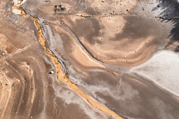 Top down aerial view of dried lake bed with abstract textures, cracked soil and small water stream. Environmental concept of drought and water shortage © AlexR