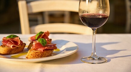 Naklejka premium Delicious bruschetta with prosciutto and glass of wine on a white table