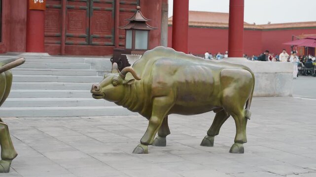 Bronze ox statue imperial courtyard red walls, weathered patina on bronze, stone steps and lantern posts, distant visitors and guides, slow tracking shot, cultural landmark vibe, Palace Museum