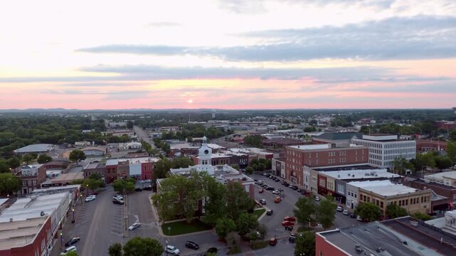 Aerial drone footage of a quaint American town square at sunset with historic buildings and a clock tower