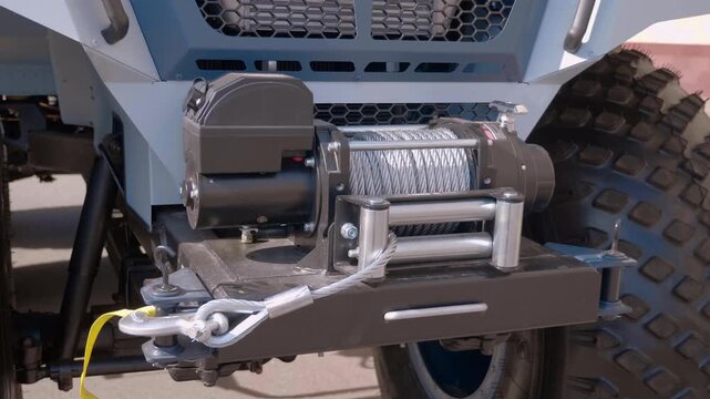 A new powerful winch on the bumper of an all-terrain vehicle, with huge wheels with off-road tread. Closeup. Shot in motion