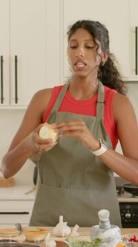 Vertical video: Inspecting cook in green apron peeling yellow onion at home kitchen, prepping meal