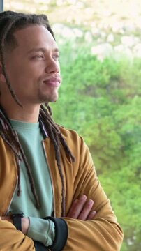 Vertical video: Smiling laughing man with locs folding arms at window, cam closing, mic, copy space
