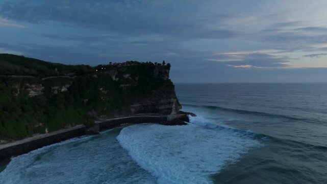 Plans drone 4K d'Uluwatu, Bali, lors de la blue hour : falaises majestueuses, oc&eacute;an Indien, lumi&egrave;res bleut&eacute;es et ciel cr&eacute;pusculaire. Id&eacute;al pour projets voyage, nature, architecture et Asie tropicale