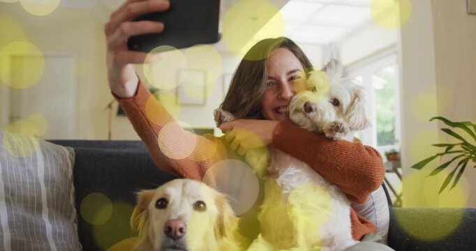Woman raising black phone and moving two dogs capturing social media selfie with gold bokeh overlay