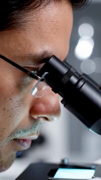 Focused Scientist Close-up of a Man Looking Through a Professional Microscope in a Laboratory for Medical Research and Scientific Discovery. Vertical. Video. Portrait Orientation.