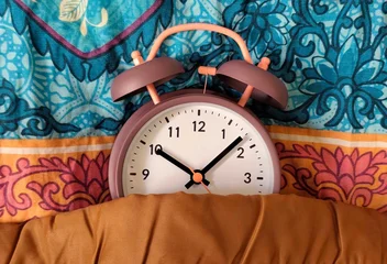 Gardinen Farbenfroh Photo of a retro twin-bell alarm clock tucked under a blanket on colorful patterned bedding, morning wake-up concept with cozy home atmosphere and vibrant textile background.  © Antonios