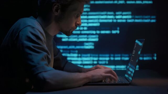Coder or data scientist working on laptop in dark office at night with blue programming script lines on background. Coding, data analytics, machine learning work process. 