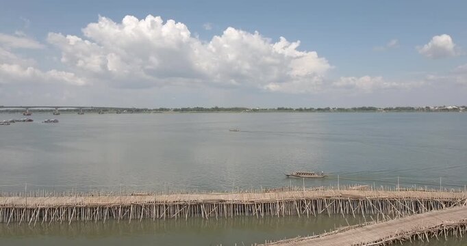 Aerial panning shot of the Kampong Cham bamboo bridge across the Mekong River, featuring motorbikes and a traditional wooden boat.
