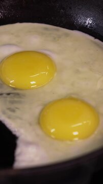A close-up of cooking fried eggs in a frying pan. Vertical video