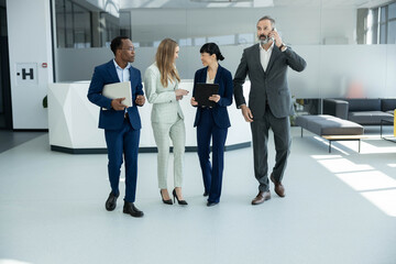 Fototapeta premium Diverse business professionals walking through a modern office building, discussing work, and communicating on mobile phones, symbolizing teamwork and corporate life