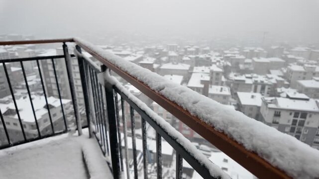 Snowfall covers city rooftops from balcony view creating winter wonderland atmosphere motion.