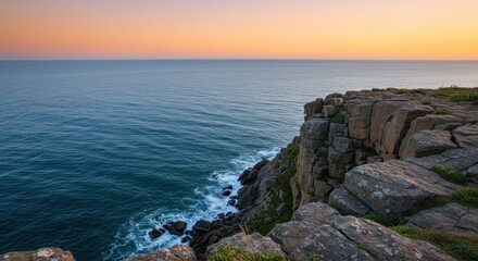 Naklejka premium Elevated rugged coastline meets tranquil ocean waters under a pastel colored sky