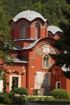 Historic red-painted Orthodox church complex of the Patriarchate of Pec, u UNESCO World Heritage site in Kosovo, surrounded by greenery under a clear blue sky