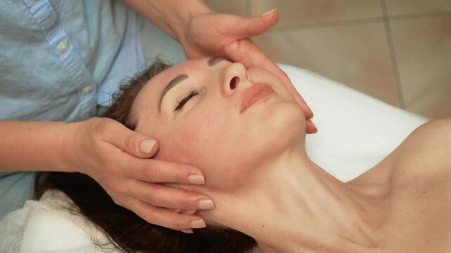 Therapist massaging jawline for relaxation and balance. Working on face to provide calming and soothing care. Professional gently stimulating jaw for rejuvenation and stress relief. Expert offering