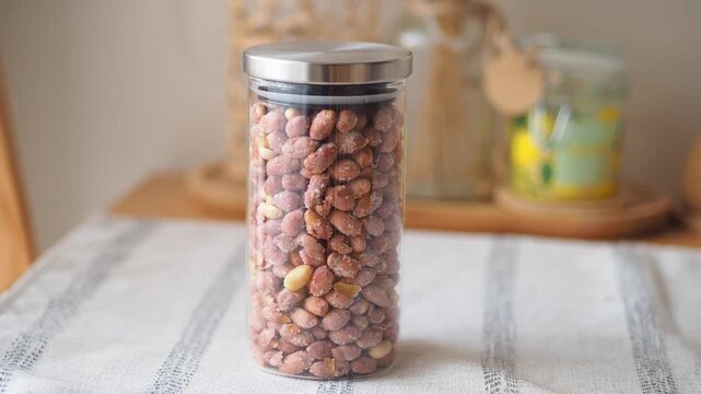 Salty roasted peanuts in glass storage jar on wooden table surface with kitchen background.