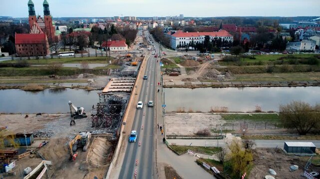 Drone aerial view flying along bridge in Poznan with pedestrians and Ostrow Tumski island and cathedral in background under cloudy sky