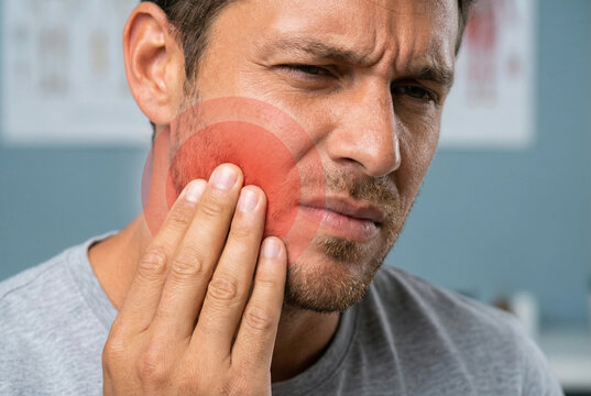 Homem brasileiro com dor de dente intensa e desconforto na mand&iacute;bula. Ponto vermelho brilhante na bochecha indicando inflama&ccedil;&atilde;o dental ou problema de sa&uacute;de