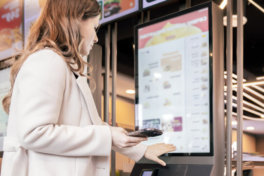 Woman selecting food on touchscreen kiosk in modern restaurant environment with intuitive digital ordering interface