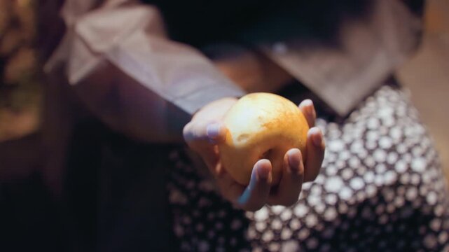 Night street closeup hand holding apple, passerby pauses to balance and toss fruit over patterned skirt, warm bokeh and soft film grain create nostalgic mood, sleeve and palm catch highlighted