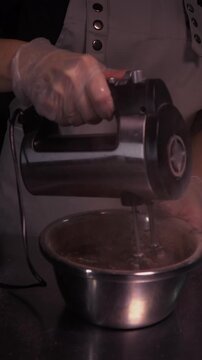 A female baker mixes eggs with flour using a mixer. A woman prepares dough for a cake or pie in a home kitchen. Vertical video.