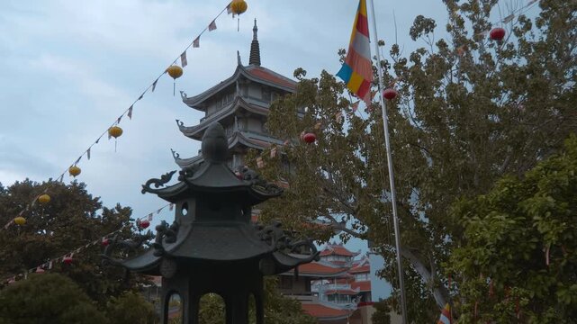 Buddhist flags and Vietnamese lanterns hang against the background of a beautiful multi-story tower of Vinh Nghiem Pagoda in Ho Chi Minh City, Vietnam with bended traditional Asian roofs and chofahs
