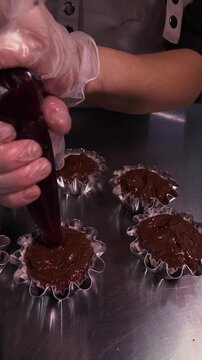 A female baker prepares cupcakes using a pastry bag. Vertical video about homemade pastries, cooking and confectionery.