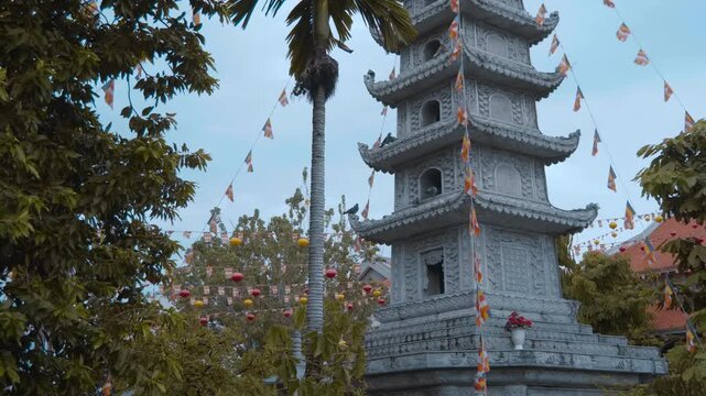 Garlands with Buddhist flags flatter on the wind attached to the Vinh Nghiem Pagoda in Ho Chi Minh City, Vietnam with palm tree growing near it