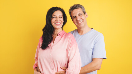 Fototapeta premium Mature couple standing together, the man embracing the woman from behind, both smiling, showing love and connection