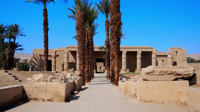 Seti I mortuary temple entrance with palm tree alley and ancient stone ruins in Luxor Egypt. Scenic pathway under vivid blue sky.