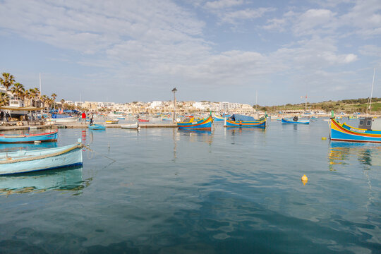 View of brightly colored traditional fishing boats bobbing gently on the tranquil, deep blue water of the harbor, Marsaxlokk, Malta.